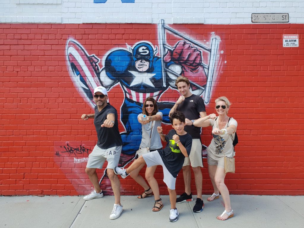 A family poing in front of a mural of Captain America on a sunny day during an Offbeat New York tour of Bushwick and Williamsburg.