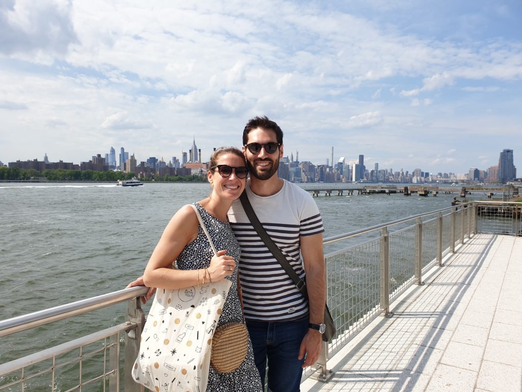 Couple in front of East River with Manhattan Skyline in the background during a offbeat New York tour in Brooklyn.